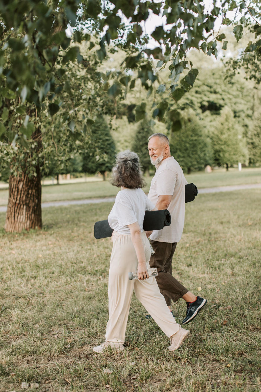 Älteres Paar spaziert mit Yogamatten durch einen grünen Park